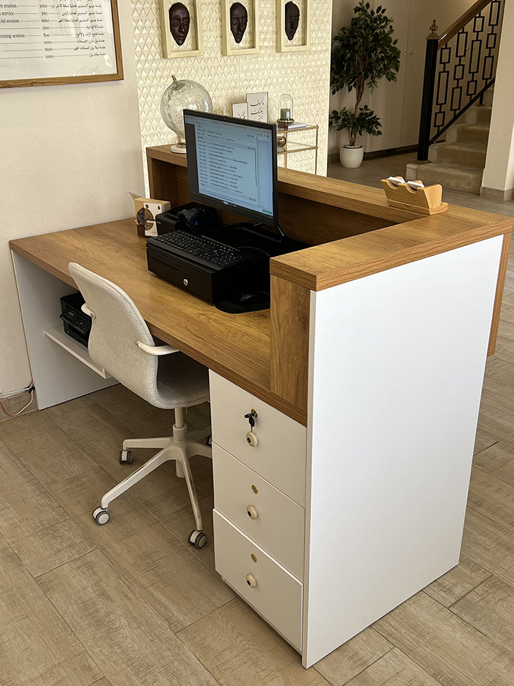 Reception desk workstation at Binan Skin Care Center with wood-finish worktop, white drawers, monitor, printer, and storage